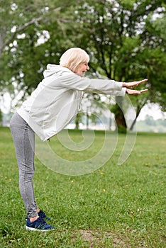 elderly sportswoman exercising on green grass in park