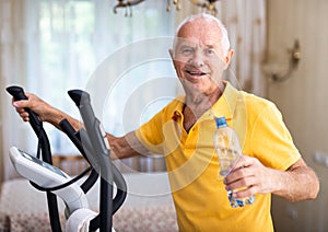 Elderly sporty man exercising on an elliptical trainer and drinking water from bottle