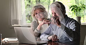 Elderly spouses using laptop laughing spend time watching funny videos