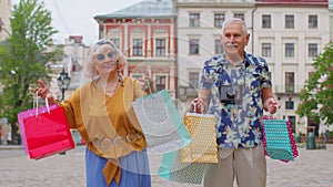 Elderly stylish couple tourists man and woman walking with colorful bags after shopping in mall