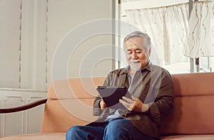 Elderly and technology concept, Happy senior asian father looking news with tablet smartphone in living room