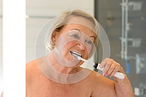 Elderly topless lady cleaning her teeth