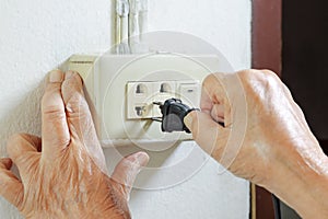 Elderly trying plug cable to the electric outlet