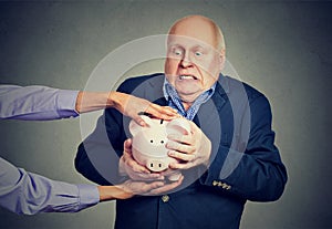 Elderly upset scared business man holding piggy bank trying to protect his savings from being stolen