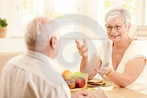 Elderly wife chatting to husband at breakfast