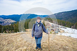 Elderly woman 60 years old hiking in mountains with snow admiring valley view