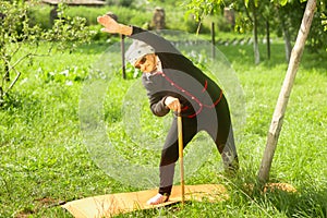 An elderly woman of 90 years old, with gray hair and a headband, doing fitness in the garden