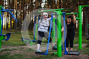 An elderly woman with an adult daughter is doing exercises on the sport playground