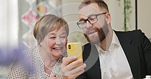 Elderly woman and adult grandson having video conversation with family . Young man teaching his grandmother making