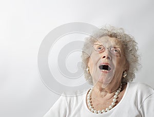 Elderly woman against a white background with her mouth open and looking up