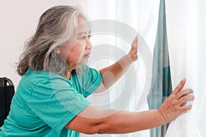 elderly woman alone at home Lonely opened the curtain at the window to see the view outside the house.