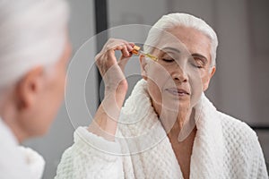 Elderly woman applying with dropper serum to face