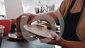 An elderly woman artist painting the clay plate with a big brush