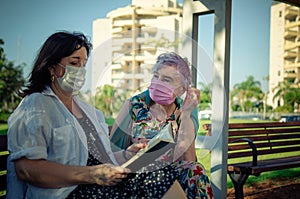 Elderly woman attentively listens to a volunteer reading a book outdoors