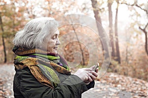 Elderly woman in an autumn park with a mobile phone