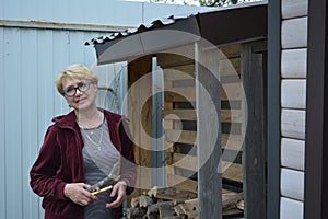 An elderly woman in a bard jacket is holding firewood for the stove.