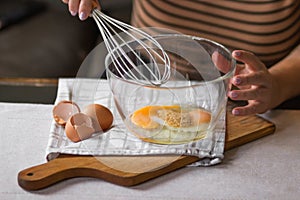 Elderly woman beats eggs with a wisk in a glass bowl. Prepare for making christmas pie or pancakes on kitchen table.