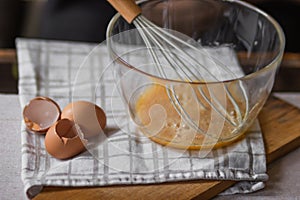 Elderly woman beats eggs with a wisk in a glass bowl. Prepare for making christmas pie or pancakes on kitchen table.