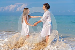 An elderly woman and beautiful girl on the beach. Grandmother granddaughter holding hands on the background of the waves of the