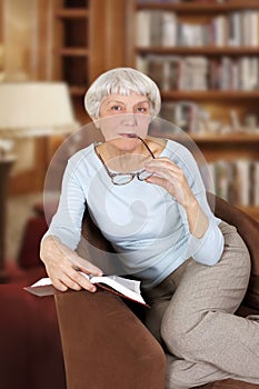 Elderly woman with book and glasses sitting in a chair