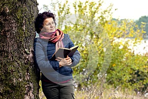 Elderly woman with a book in her hands on the nature. Reading in nature. Rest in the woods. Reading the Bible. Unity with nature