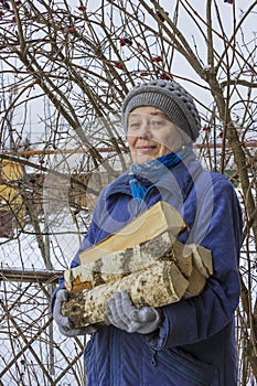 An elderly woman carries an armful of firewood in her hands