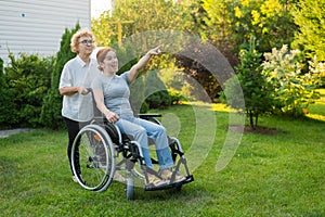 An elderly woman is carrying an adult daughter sitting in a wheelchair. Caucasian woman pointing her finger admiringly photo