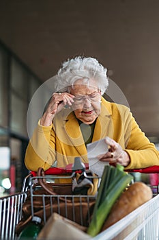 Elderly woman checking her receipt after purchase, looking at amount of money spent, ensuring all charges are correct.