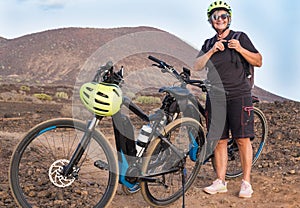 The elderly woman checks the yellow helmet and the backpack before starting the off-track route with bici. Outdoor in mountain.