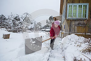 Elderly woman cleans the snow near his home.