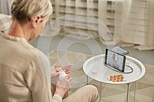 An elderly woman communicates remotely via a tablet with her doctor and takes medications according to his