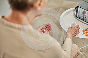 An elderly woman communicates remotely via a tablet with her doctor and takes medications according to his