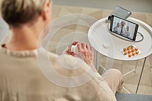 An elderly woman communicates remotely via a tablet with her doctor and takes medications according to his recommendations.