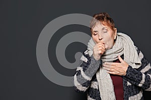 Elderly woman coughing against dark background.