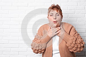 Elderly woman coughing near brick wall.