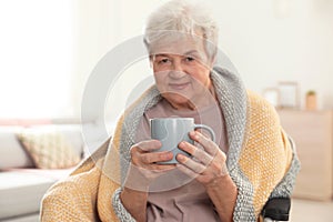 Elderly woman covered with blanket drinking tea at nursing home