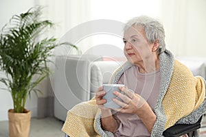 Elderly woman covered with blanket drinking tea at nursing home. Assisting senior people