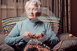 Elderly woman, crocheting on chair at home, creative leisure