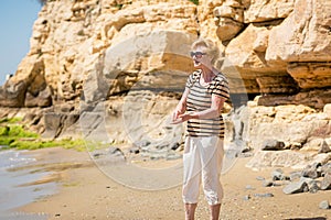 Elderly woman in dark sunglasses feeds seagulls on the rocky beach