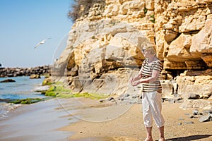 Elderly woman in dark sunglasses feeds seagulls on the rocky beach