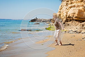 Elderly woman in dark sunglasses feeds seagulls on the rocky beach
