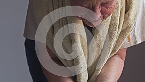 An elderly woman with a delina in her hair washes her face with a towel around her neck. Splashes water in the face