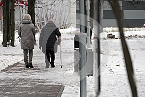 An elderly woman with disabilities walks in the park in winter, accompanied by her daughter.