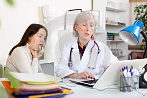 Elderly woman doctor writing prescription for female patient complaining of sore throat