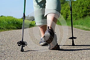 Elderly woman does Nordic Walking on an asphalted field road. Female legs with Nordic Walking poles on a cartway