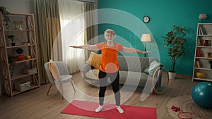 An elderly woman does a warmup before training. The greyhaired woman raises her arms above her head and reaches up