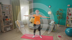 An elderly woman does a warmup before training. The greyhaired woman raises her arms above her head and reaches up