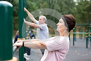 Elderly woman doing exercises in sports bars on outdoor sports ground