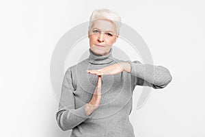 Elderly woman doing a timeout gesture on grey background photo