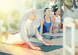 Elderly woman doing upward facing dog pose in yoga studio